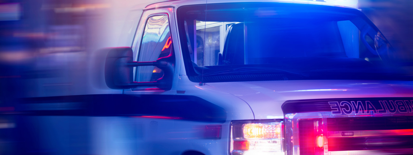 Front view of an ambulance with flashing lights in an urban setting, conveying urgency and speed.